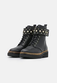 Botas negras de cuero hasta el tobillo con un puño desmontable con tachuelas, detalles dorados y un cierre de cremallera dorada a lo largo de la suela. Cierre con cordones.