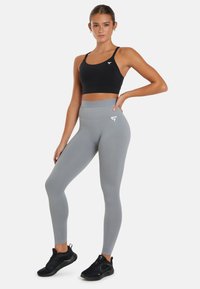 Grijze high-waisted leggings met een strakke pasvorm, gecombineerd met een zwarte sportbh. Beide zijn gemaakt van rekbaar materiaal en hebben een logo-accent.