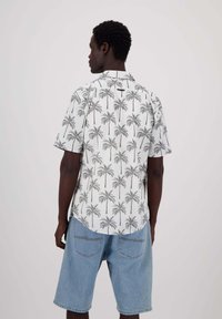 Camicia a maniche corte con sfondo bianco e stampa di palme nere, abbinata a pantaloni corti in denim azzurro. Design minimalista, vestibilità rilassata.