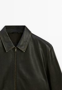 Black leather jacket featuring a pointed collar and a front zipper. The texture is smooth with a natural grain, showcasing a sleek design.