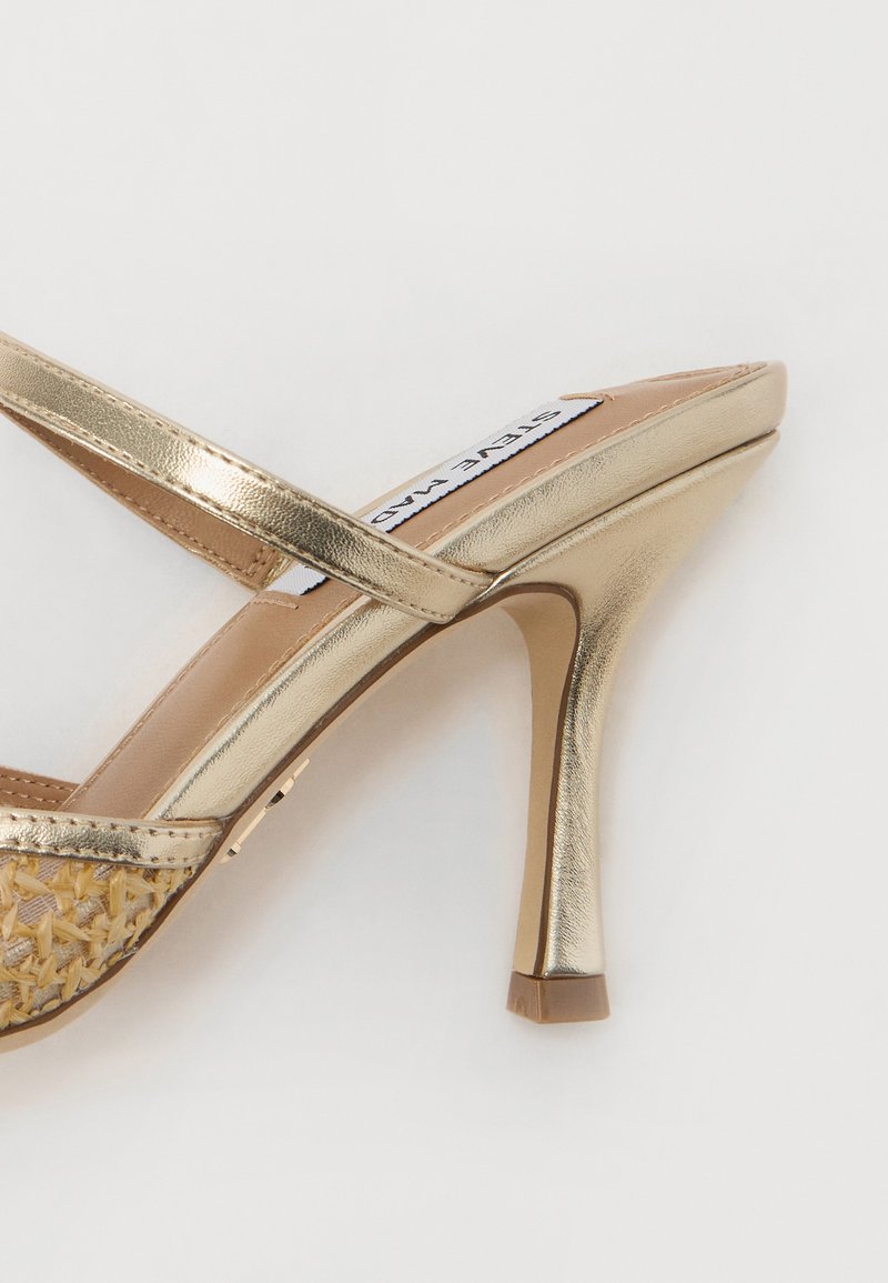 Goldfarbene metallische High-Heelsandale mit gekreuzten Riemen, einem geflochtenen Fußbett und einer spitzen Zehenpartie. Der Absatz ist schlank und etwa 7,5 cm hoch.