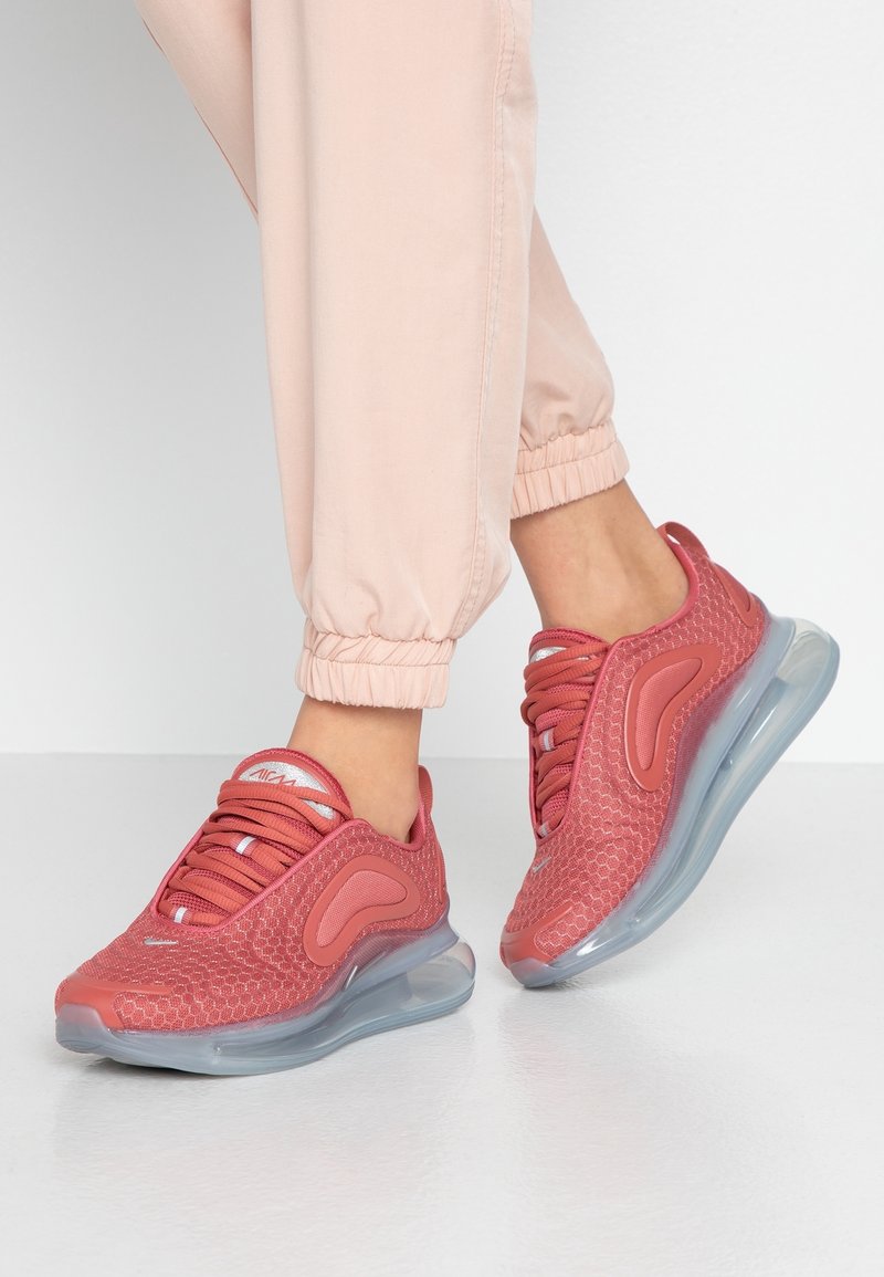 Röda träningsskor med övre del i nät, rundad tå och en genomskinlig luftkuddesula. Skosnören i samma färg som skon med ett texturerat mönster.