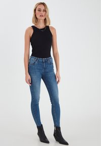 Melnā bezpiedurkņu bodija kombinācija ar ziliem skinny džinsiem. Džinsiem ir klasiskā piecu kabatu dizains un viegla nolietošana. Melnas potīšu zābaki.