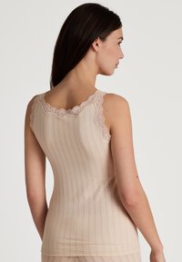 Nude tanktop met kantafwerking, met een verticale ribbelpatroon. Zachte textuur met een aansluitende pasvorm en brede bandjes.