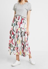Una falda larga y fluida presenta un patrón abstracto en rosa, verde y azul sobre un fondo blanco. Combinada con una camiseta gris y zapatillas blancas.