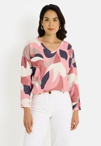 Top rosa de manga larga con un patrón abstracto multicolor, que presenta un escote en V y una tela texturizada. Combinado con pantalones blancos.