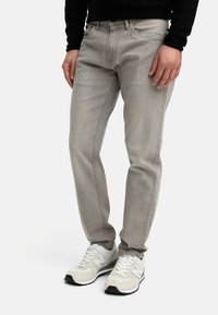 Light grey denim jeans with a slim fit, featuring side and back pockets, stitched detailing, and worn looking fabric texture.