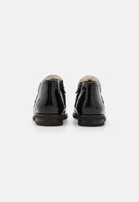 Zapatos de charol negros con un acabado suave, cierre de cremallera y forro de felpa, con un tacón bajo y un diseño de punta redonda.