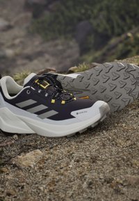 Chaussures de randonnée imperméables noires et blanches avec semelles robustes reposant sur une surface de gravier en plein air.
