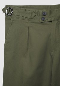 Olivgrüne Hose aus strukturiertem Stoff, mit einem vorderen Schnallenverschluss, Falten und zwei Taschen. Zwei-Knopf-Verschluss an der Taille.