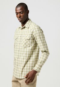 Camicia a quadri verde chiaro con maniche lunghe, due tasche sul petto e chiusura a bottoni. Presenta un sottile motivo a scacchi e una vestibilità regular.