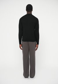 Čierny sveter s priliehavým strihom, okrúhlym výstrihom a dlhými rukávmi, v páre so sivými širokými nohavicami a bielymi teniskami.