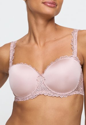 Frau trägt einen hellrosa Spitzen-BH mit glatten Körbchen und floralen Spitzen-Details an Trägern und Bund.