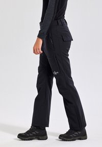 Zwarte buitenbroeken gemaakt van duurzaam materiaal, met meerdere zakken, ritsen en een slim-fit ontwerp. Gecombineerd met zwarte wandelboots.