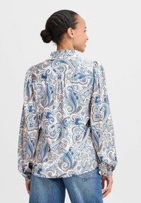 Blusa a maniche lunghe in motivo paisley blu e beige, con colletto arricciato, spalle plissettate e polsini elastici. Tessuto misto cotone.