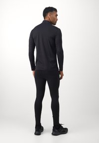 Svart treningstopp med lange ermer og høy krage, kombinert med svarte tights. Stoffet ser glatt og tettsittende ut, med en subtil tekstur.