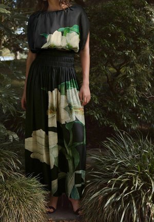 Robe noire avec des manches courtes bouffantes. Présente un grand imprimé floral blanc et des feuilles vertes. Taille smockée et jupe fluide.