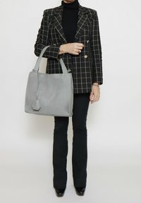 Borsa a mano in pelle grigia con design strutturato, caratterizzata da doppie maniglie e un accento geometrico. Texture sottile, forma rettangolare, dettagli minimali.