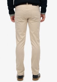 Chinos de algodón beige con un corte ajustado, que cuentan con cinco bolsillos, yugo trasero y costura en contraste, llevados con zapatos negros.