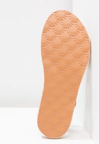 Semelle de chaussure beige avec un motif texturé présentant des formes rayonnantes. La semelle est plate et légèrement courbée sur les bords.