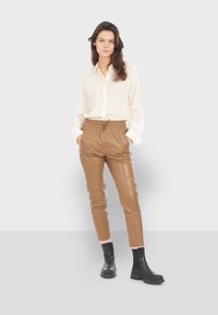 Kremasta košulja na dugme, smešane kožne joga hlače s elastičnom smešnom linijom, i crne čizme do gležnja s debelim potplatima; glatka tekstura i prilagoden dizajn.