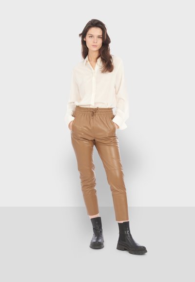 Chemise à boutons crème, pantalon de jogging en cuir marron avec taille élastique et bottines noires à semelles épaisses ; texture lisse et design ajusté.