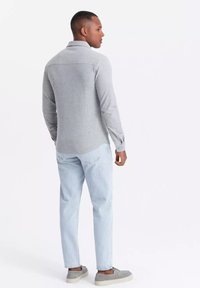 Camisa gris de manga larga con una textura suave, que presenta un cuello y detalles de botones, combinada con jeans azul claro y zapatos grises.