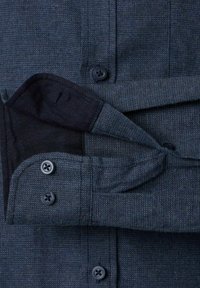 Close-up van een donkerblauwe gestructureerde stoffen mouw van een shirt met twee marineblauwe knopen, waarvan één dichtgeknoopt en één los hangt, waardoor de binnenvoering zichtbaar is.