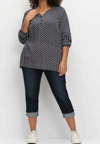 Tmavě modrá blůza se vzorem a tříčtvrtečními rukávy, v kombinaci s tmavě modrými džíny s ohrnutými manžetami a bílými teniskami.