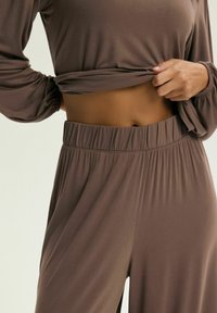 Brązowy zestaw do wypoczynku z luźną bluzą z długim rękawem i szerokimi spodniami. Wykonany z miękkiego materiału, z elastycznym pasem i ściągaczami przy mankecie.