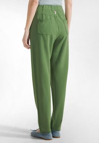 Grønne, løstsiddende bomuldsbukser med høj talje, to baglommer og et simpelt design. Udstyret med en lyserød etikette ved taljebåndet.