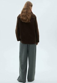 Giacca oversize marrone in misto lana con schiena dritta, abbinata a pantaloni a gamba larga grigi a vita alta, caratterizzati da una texture morbida.