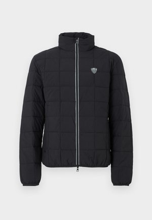 Veste matelassée noire avec col montant, fermeture à glissière frontale et poignets élastiques. Comprend un logo sur la poitrine gauche et un détail de fermeture éclair contrastant.