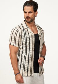 Kurzarmhemd aus gewebtem Stoff, mit cremigem Hintergrund und schwarzen vertikalen Streifen sowie durchbrochenen Mustern, kragenförmiges Design.