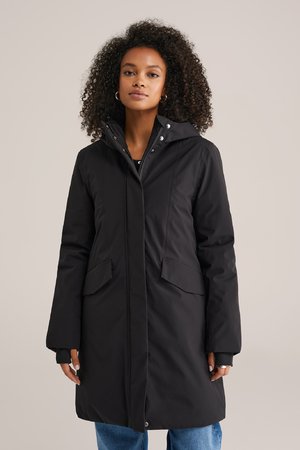 Parka nera isolata con cappuccio, dettagli in bottoni e due tasche frontali. Il design presenta una silhouette dritta e chiusura con bottoni.