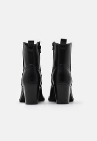 Botines de tacón negro hechos de cuero suave, con cierre de cremallera, punta redonda y un robusto tacón cuadrado para mayor estabilidad.