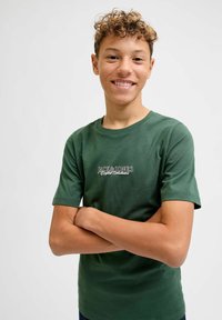 Groene katoenen t-shirt met korte mouwen, met een logo aan de voorkant in witte en zwarte tekst. De stof heeft een gladde textuur en een klassieke snit.