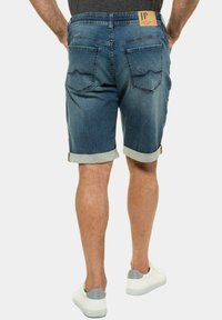 Shorts de mezclilla en un tono azul medio con dobladillos vuelta, que cuentan con dos bolsillos traseros con un patrón de olas y un parche con el logo en la cintura.