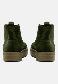 Botas de tobillo de ante verde con un acabado texturizado, que cuentan con una suela de plataforma marrón y paneles laterales elásticos para facilitar su uso.