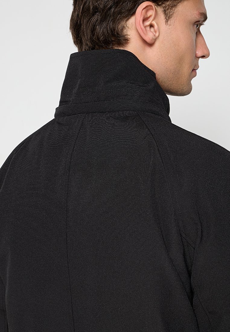 Zwarte jas met een hoge kraag, textuurmateriaal en een gestroomlijnd ontwerp. De achterkant toont verticale naaddetails en een nette afwerking.