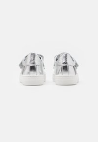 Sneakers metallici argento con superficie testurizzata, suola in gomma bianca e lacci piatti. La vista posteriore mostra il collare imbottito e gli accenti del tallone lisci.