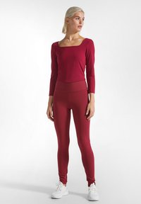 Bordeauxrode top met lange mouwen en vierkante halslijn, gecombineerd met bijpassende leggings; gladde textuur; nauwsluitend model; witte sneakers.