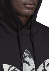 Felpa con cappuccio nera con un grande logo mimetico bianco e grigio, strutturato, sul davanti. Presenta lacci e un tessuto morbido.