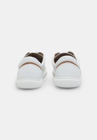 White leather shoes with rounded backs, brown accents, and textured soles; minimalistic design with a smooth finish and stitched details.