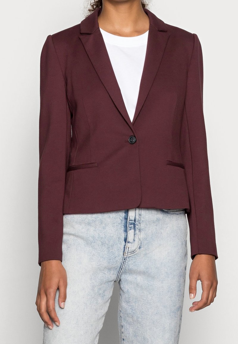 Blazer bordeaux ajusté avec revers crantés, fermeture à un bouton, deux poches latérales et manches longues, associé à un t-shirt blanc et un jean clair.