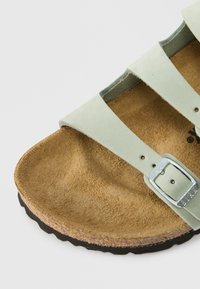 Μαλακή πράσινη δερμάτινη σάνδαλη με ρυθμιζόμενο κούμπωμα, φιλικό προς το περιβάλλον πέλμα από φελλό και υφασμάτινη, υφή καφέ σουέτ εσ ωτερική σόλα. Μαύρη καουτσούκ εξωτερική σόλα με οδοντωτές άκρες.