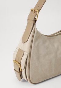 Μπεζ σουέτ τσάντα χεριού με λείο δερμάτινο λουράκι και χρυσές λεπτομέρειες. Διαθέτει καμπυλωτό σχήμα και μηχανισμό με κούμπωμα στο λουράκι.