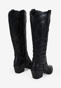 Botas de cuero negro hasta la rodilla con patrones circulares de remaches, una cremallera lateral y un tacón grueso para mayor estabilidad.
