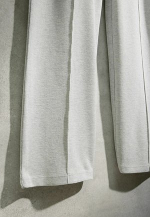 Közelkép világosszürke bordázott kötött anyagról, amely lóg, egyenletes szegélyekkel és lágy textúrával semleges háttér előtt.