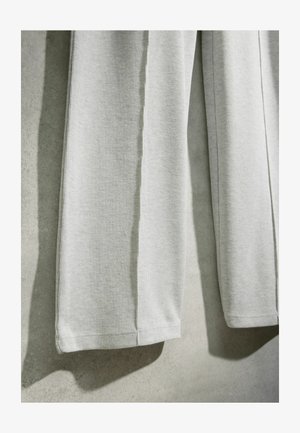 Közelkép világosszürke bordázott kötött anyagról, amely lóg, egyenletes szegélyekkel és lágy textúrával semleges háttér előtt.